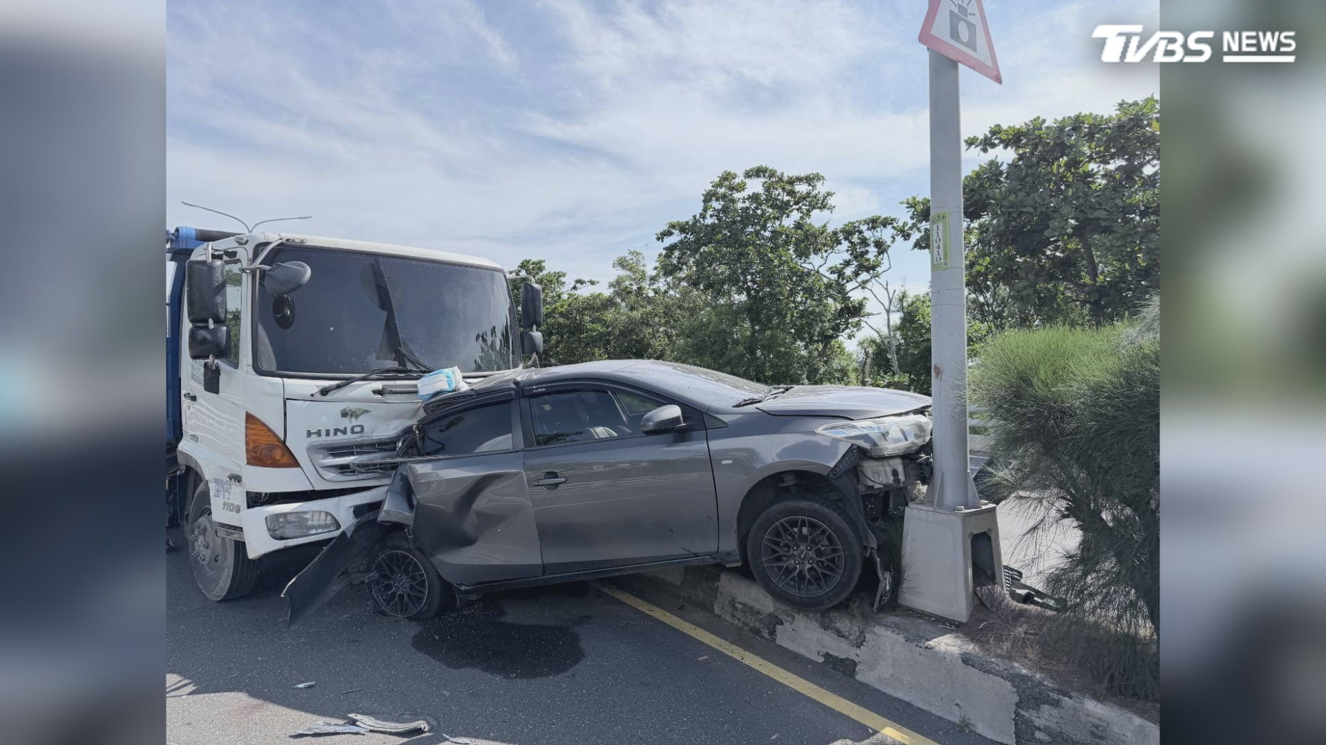 休旅車車尾嚴重凹陷，被推擠上分隔島後，前保險桿也已毀損，整部車被夾擊在大貨車和路燈桿中間，形同夾心餅乾（圖／TVBS）