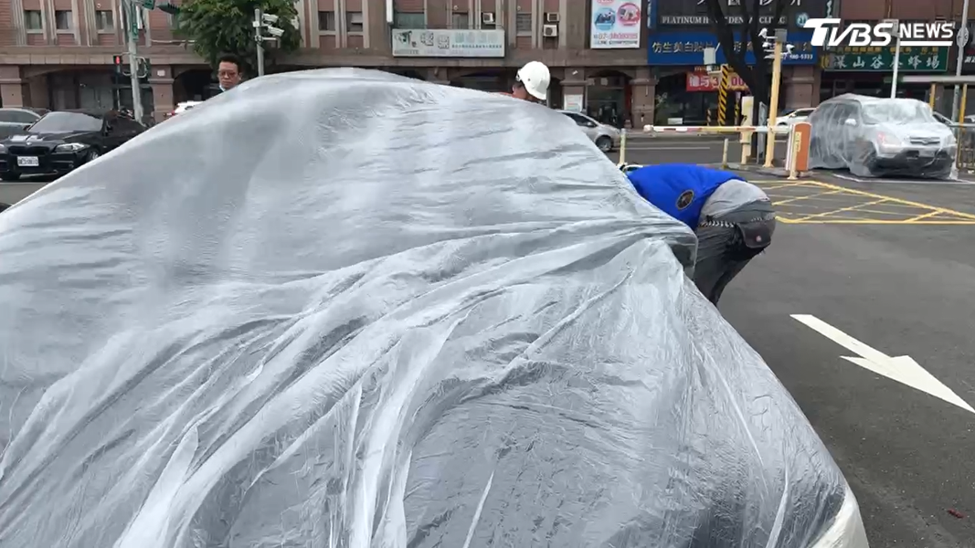 現場風勢相當大,施工人員分工合作,小心翼翼地將大型塑膠袋套在每一輛車上,塑膠套好幾度差點被強風吹掀。(圖/TVBS)