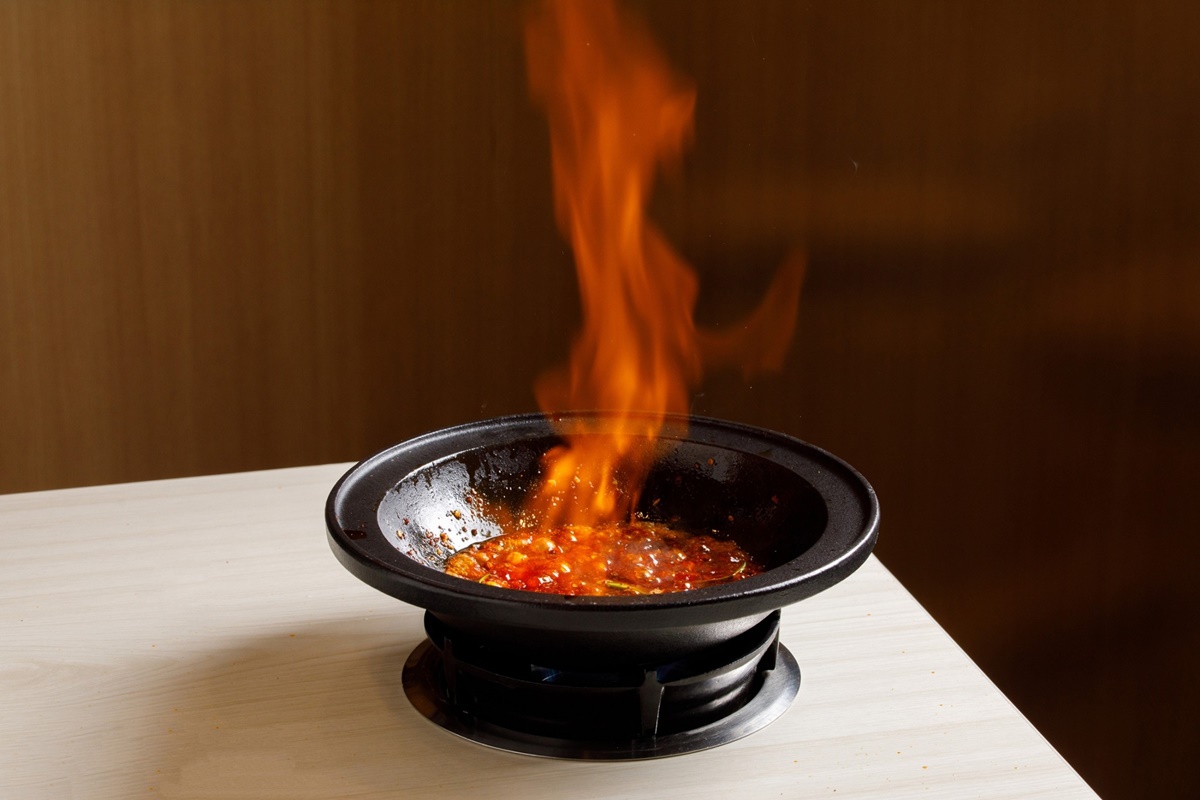 桌邊炒香麻辣底料,再加入米酒點火燃燒,辛香料風味十足。(圖/業者提供)
