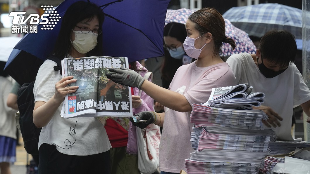 這位女性讀者撐著傘,買了兩份最後一期香港蘋果日報。(圖/達志影像美聯社)