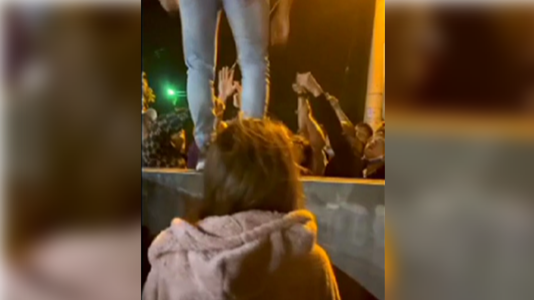 一名男子站在矮牆上,向下方民眾嗆聲。(圖/翻攝自記者爆料網)