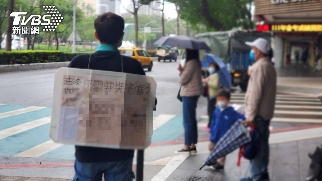 簡姓男子身上背著自製廣告厚紙板,站在街頭引人好奇多看一眼。
