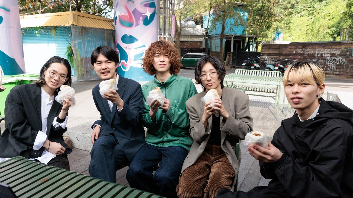 左起為⿎⼿Sho、鍵盤⼿Rosa、擔任DJ的Ofeen、⾙斯⼿Zum、主唱Hiyn，團員一起吃刈包。（圖／華納音樂國際部JPOP提供）