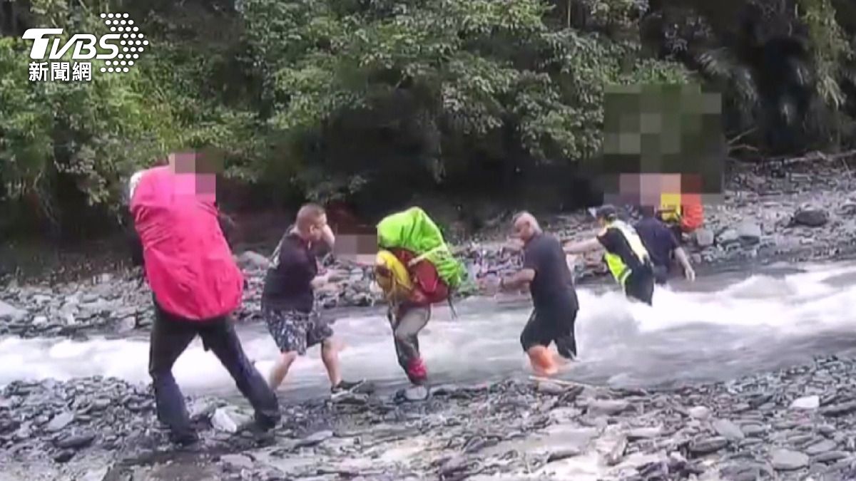 登山客們揹著大型登山包重裝前行，警方人員則在湍急的溪流中站立成為「水柱」。(圖／消防隊提供)
