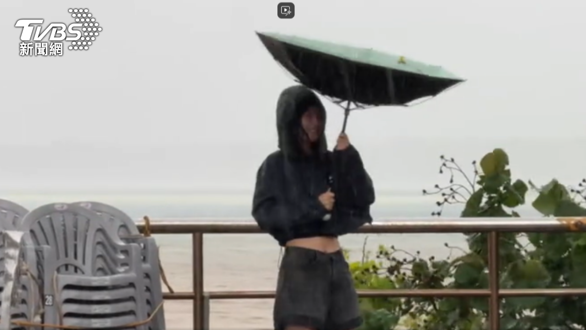 遊客在南灣岸邊冒雨觀浪，雨傘被吹開花。（圖／TVBS）