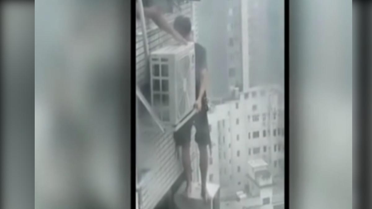 強颱樺加沙襲港期間,男子冒著狂風暴雨爬出窗外加固冷氣。(圖/上海東方衛視)