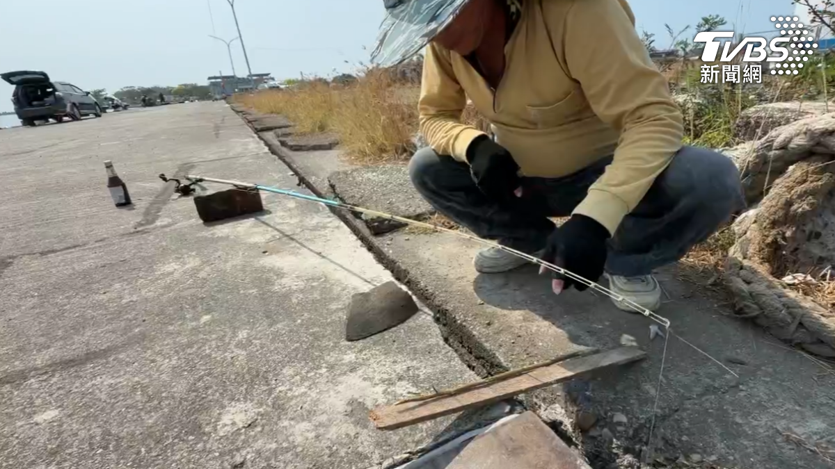 高雄興達港油庫有釣客捨棄傳統岸邊釣點,將釣竿伸入水泥地上的一道隙縫中垂釣。(圖/TVBS)