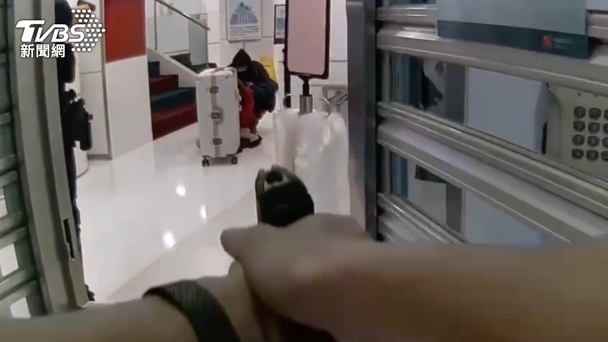 警方進入銀行時，嫌犯挟持女行員躲在行李箱後方與警方對峙。（圖／TVBS）