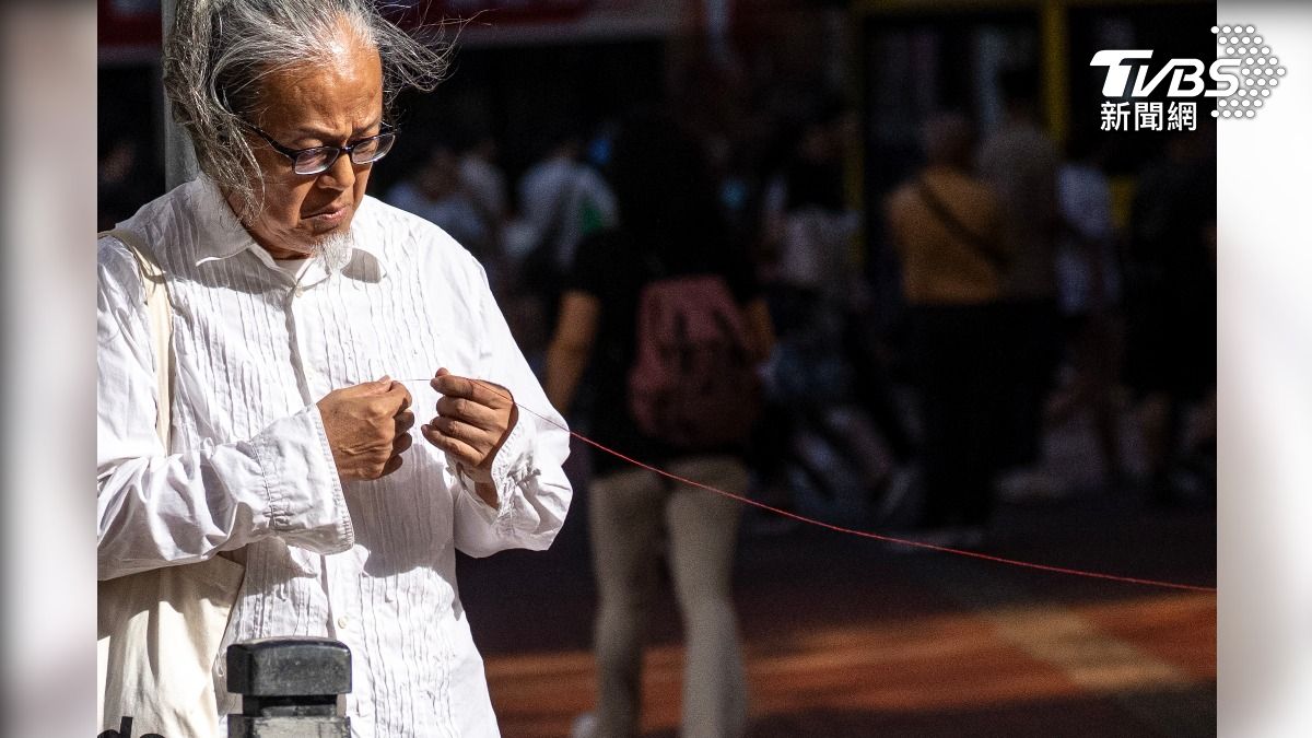 香港行為藝術家三木(陳式森)在香港東角道進行行為藝術創作,嘗試將一條6.4公尺長的紅線綁在路牌上。(圖/ 達志影像美聯社)