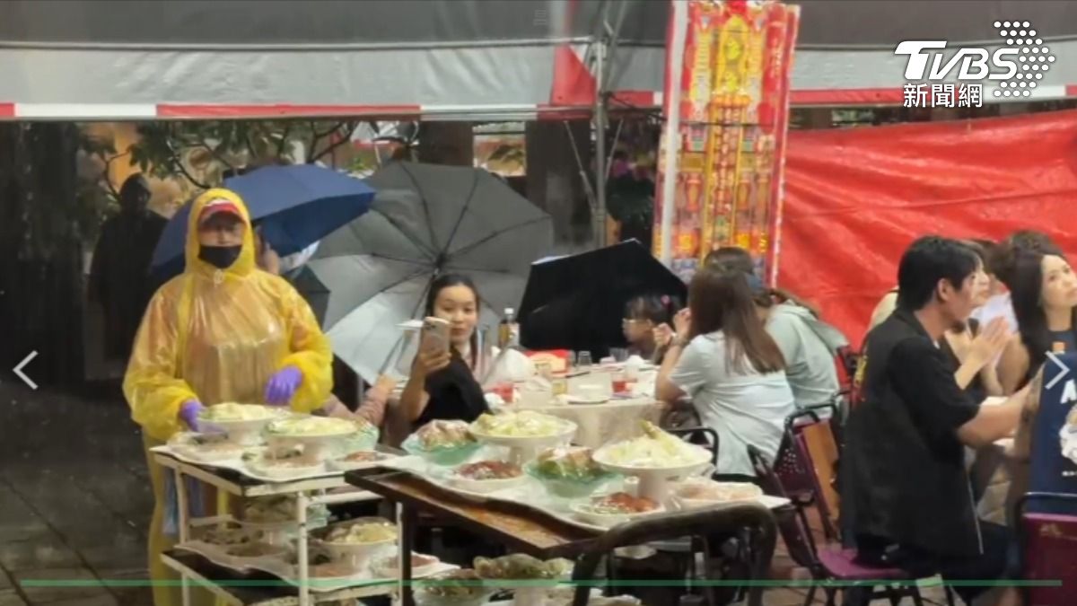 台南市中西區晚間時雨量一度出現50毫米,當地宮廟宴席,工作人員還得穿雨衣送菜。(圖/TVBS)