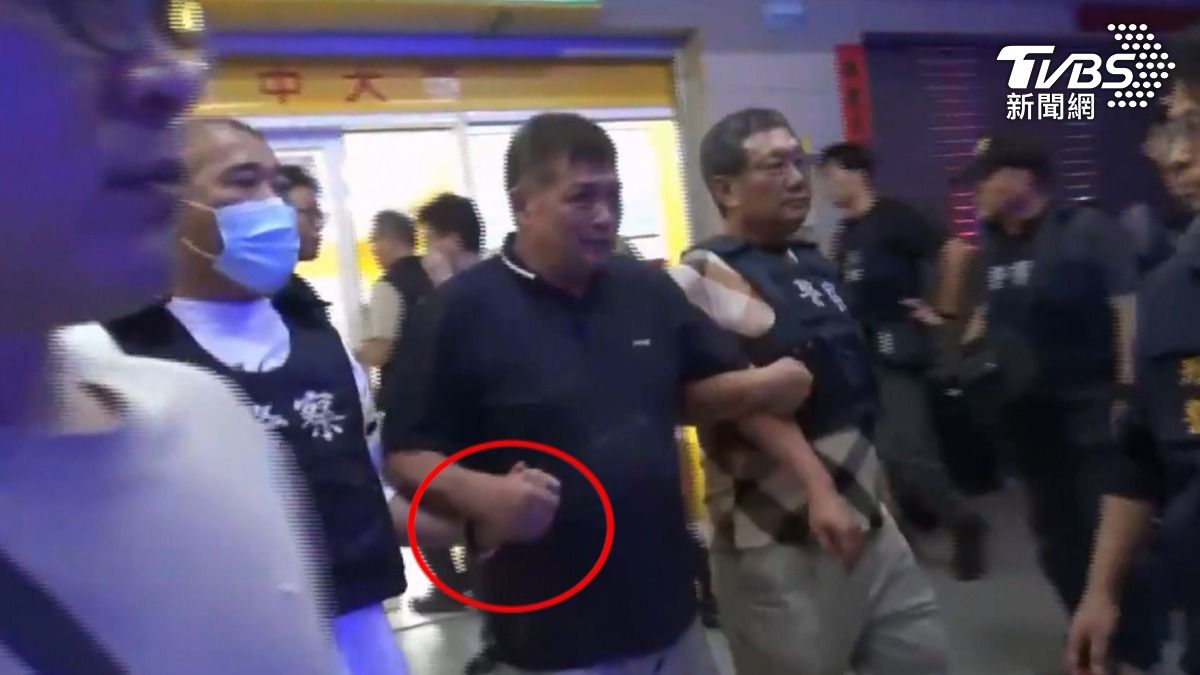 宮廟董事長和蔡政宜兩人穿上防彈背心,一左一右牽著嫌犯走出彩券行,蔡政宜還和嫌犯十指交扣。(圖/TVBS)