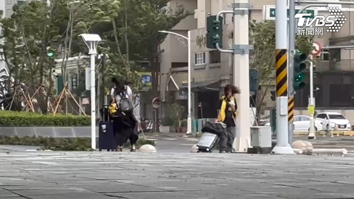 巴威颱風逐漸逼近,拖著行李的旅客,在高雄知名地標85大樓旁,被強風吹到一度走不穩,一度停下靠在電桿,防止被吹走(圖/TVBS)