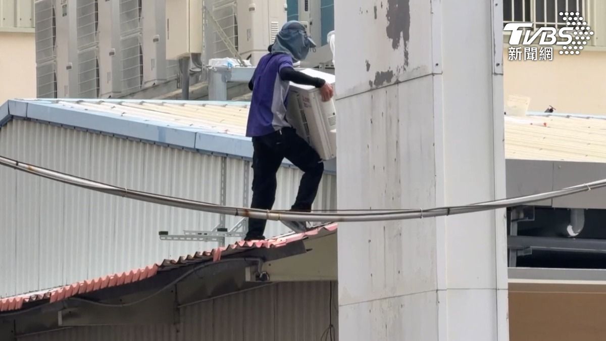 高雄一名工人獨自站在鐵皮屋簷上搬運冷氣室外機，卻未配戴安全帽及防墜安全帶。（圖／TVBS）